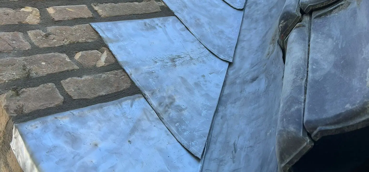 Nieuw loodwerk langs een schoorsteen en dakpannen voor waterdichte dakrenovatie.