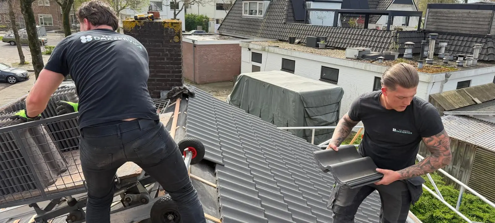 Twee dakdekkers plaatsen nieuwe zwarte dakpannen op een schuin dak met houten latten ondergrond.