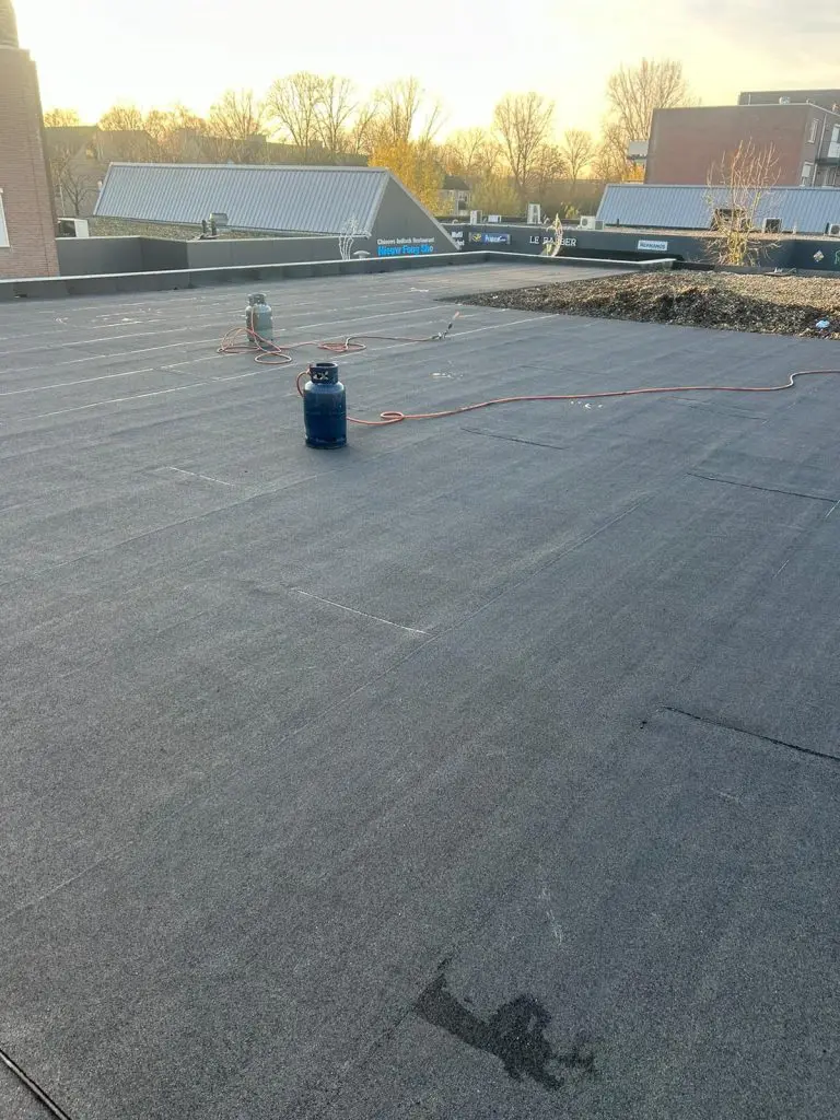 Plat dak met nieuw aangebracht bitumen dakbedekking en gasflessen voor het branden van de dakbedekking.