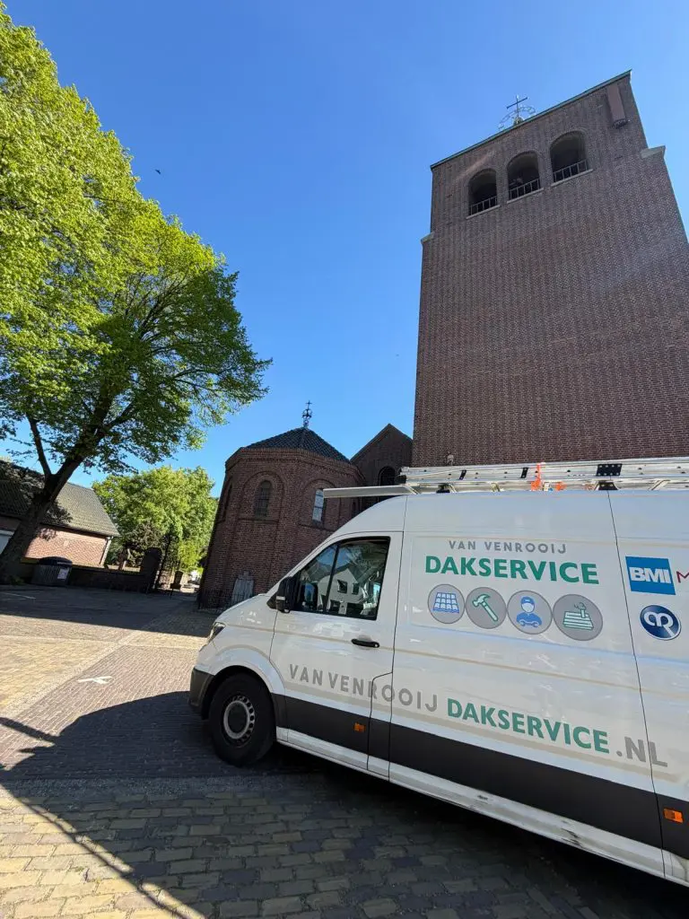 Bestelwagen Van Venrooij Dakservice geparkeerd bij kerkgebouw met dakpannen onder blauwe lucht en groene bomen