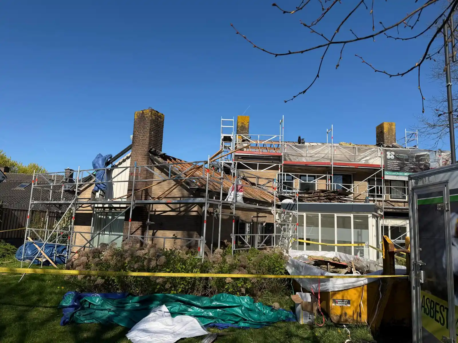 Dakwerk in uitvoering met steigers rondom huis en dakpannen verwijderd voor renovatie onder blauwe lucht.