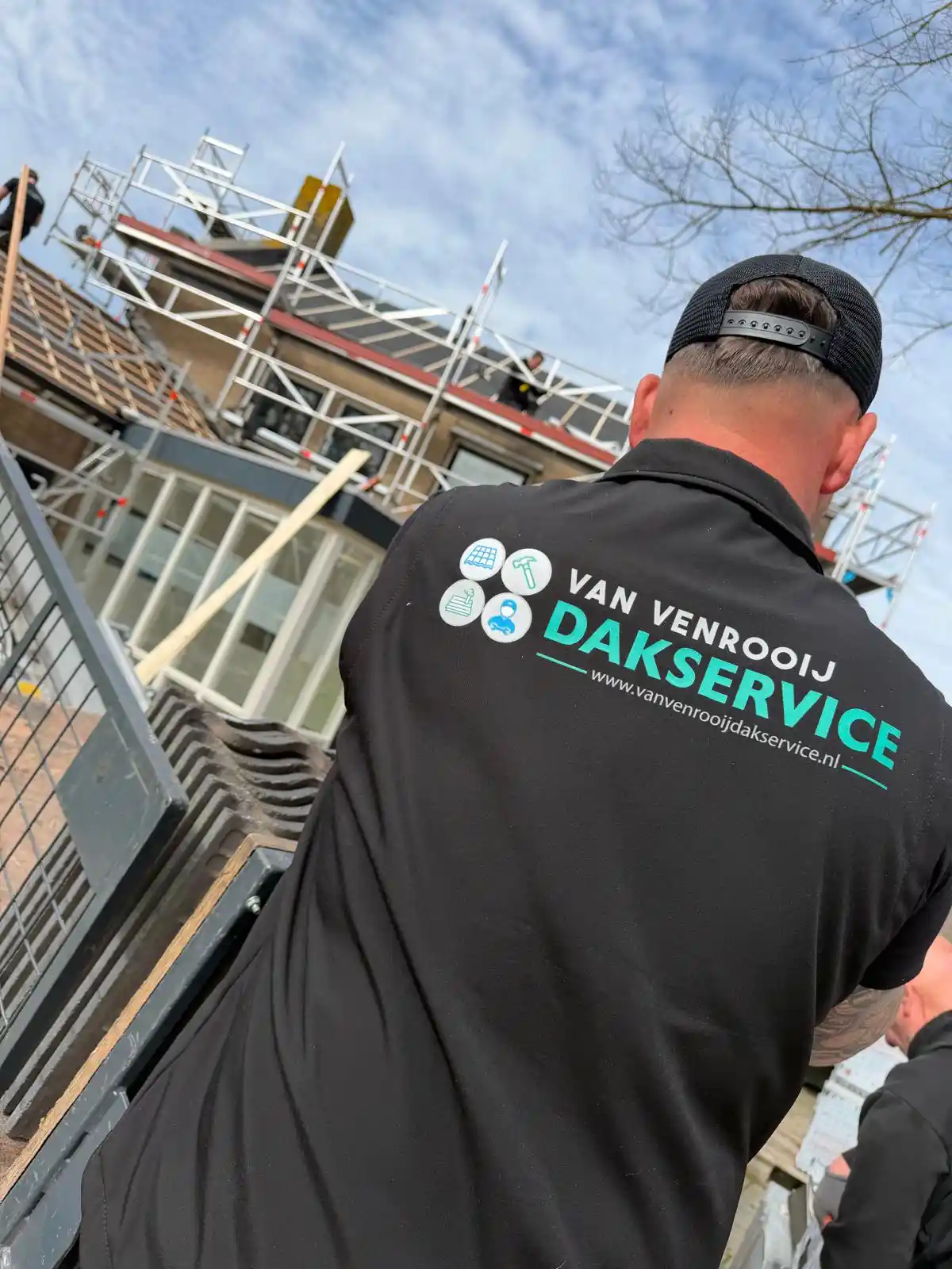 Dakdekker met Van Venrooij Dakservice shirt bij woning met steiger en dakbedekking in uitvoering.