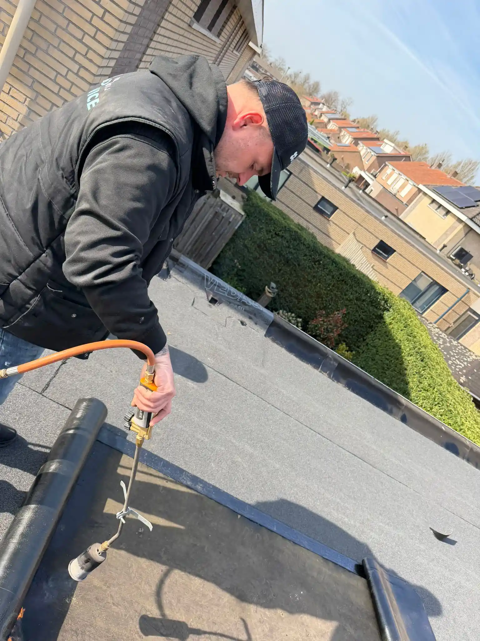 Dakdekker brandt bitumen met gasbrander op plat dak tijdens dakwerkzaamheden bij woonhuis.